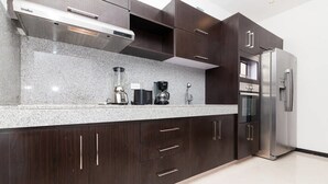 A modern kitchen with dark wood cabinets, a granite countertop, a built-in oven, and a stainless steel refrigerator. - Heliko 104B by CocoBR (Playa del Carmen)