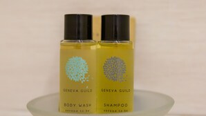 Two bottles of Geneva Guild body wash and shampoo on a clear glass stand. - BH Napoli Railway (Naples)