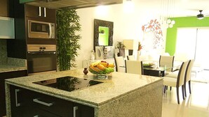 A modern kitchen with a granite countertop, built-in appliances, and a dining area with a green accent wall. - Heliko 102 by CocoBR (Playa del Carmen)