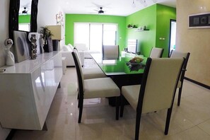 Un espace repas moderne avec une table en verre, des chaises blanches et un mur d’accent vert.