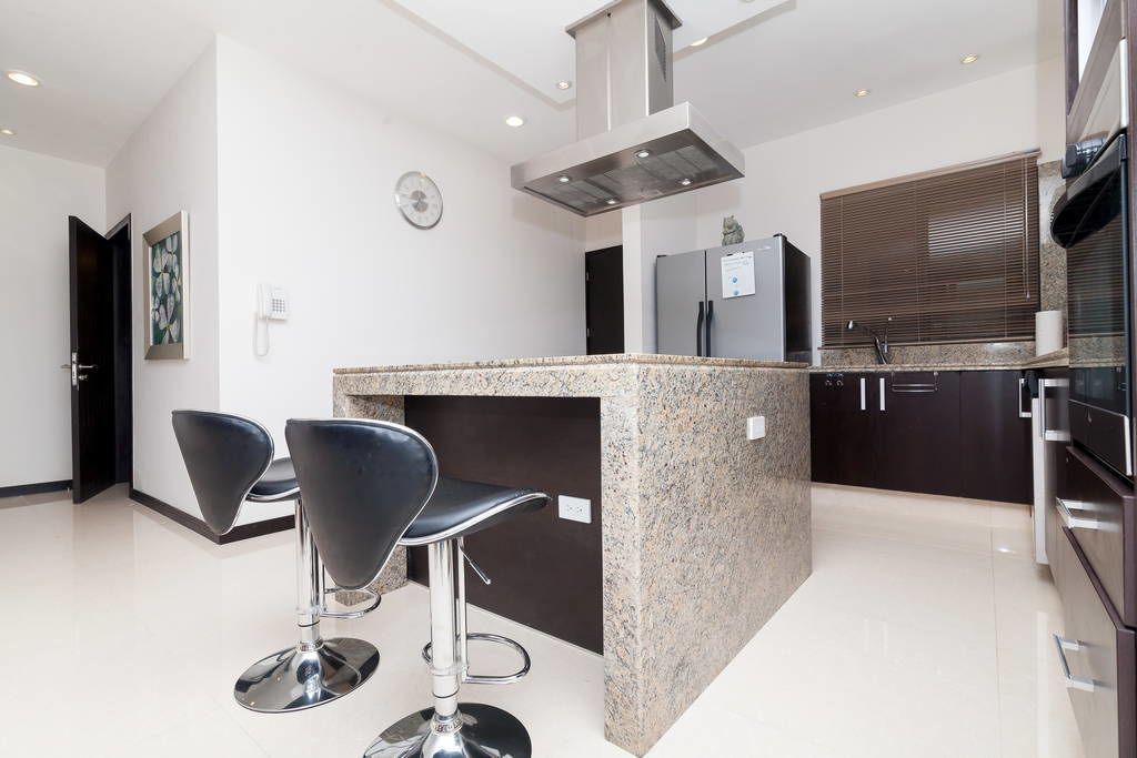 A modern kitchen with two black bar stools, a stainless steel range hood, and a built-in refrigerator.