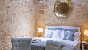 A stone-walled bedroom with a bed, two upholstered chairs, and a decorative mirror. - Lemon Tree Relais by CX Collection (Zabbar)