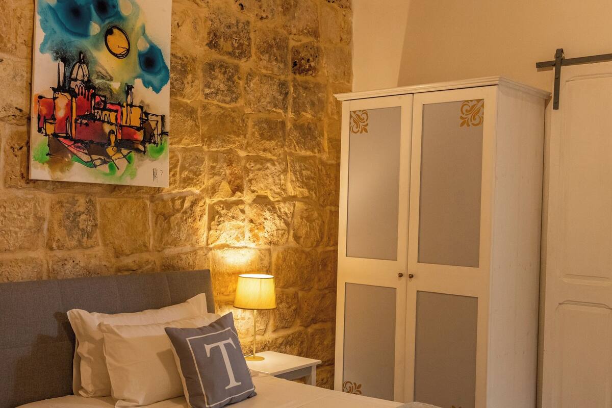 A room with a stone wall, a bed with a headboard, a wardrobe, and a painting on the wall.