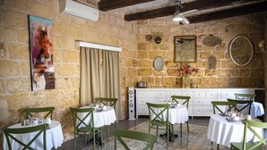 A dining area with round tables, green chairs, and a stone wall. - Lemon Tree Relais by CX Collection (Zabbar)