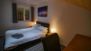 A hotel room with a bed, a nightstand, a chair, a window with curtains, and a wall painting.