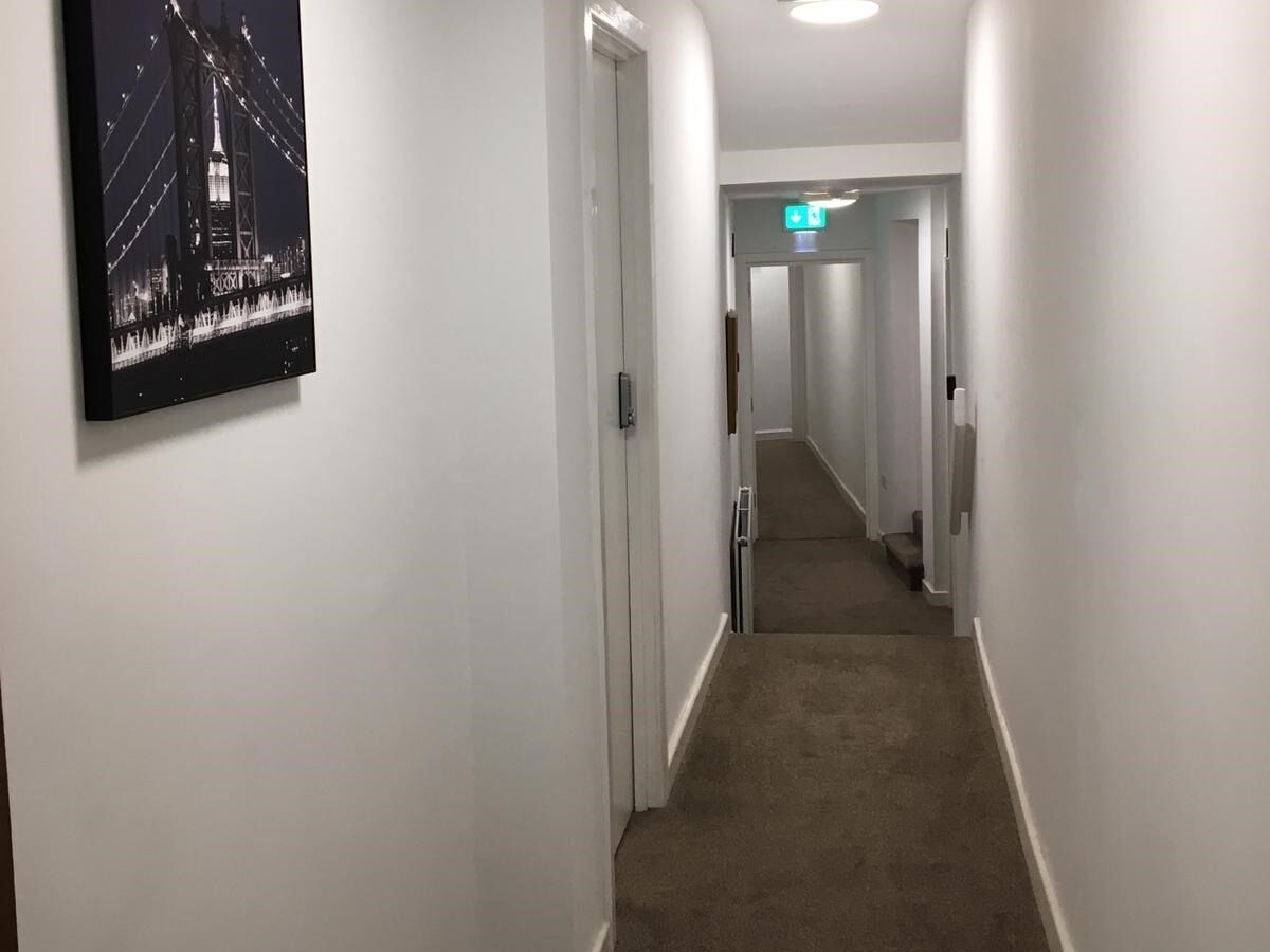 A narrow, carpeted hallway with white walls and doors, leading to a staircase.