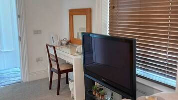 A bedroom with a bed, a desk, a television, and a window with blinds.