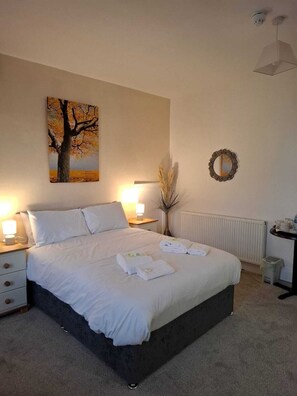 A neatly made bed with white linens and towels, a painting of a tree, a mirror, and a radiator. - The Dalbury and Palmer (Sheffield)