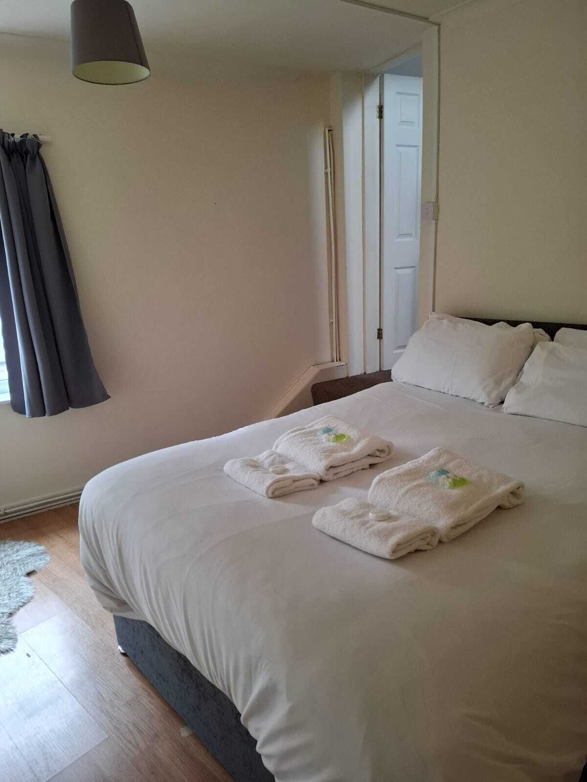 A neatly made bed with two folded towels, a dark curtain, and a light-colored wall.