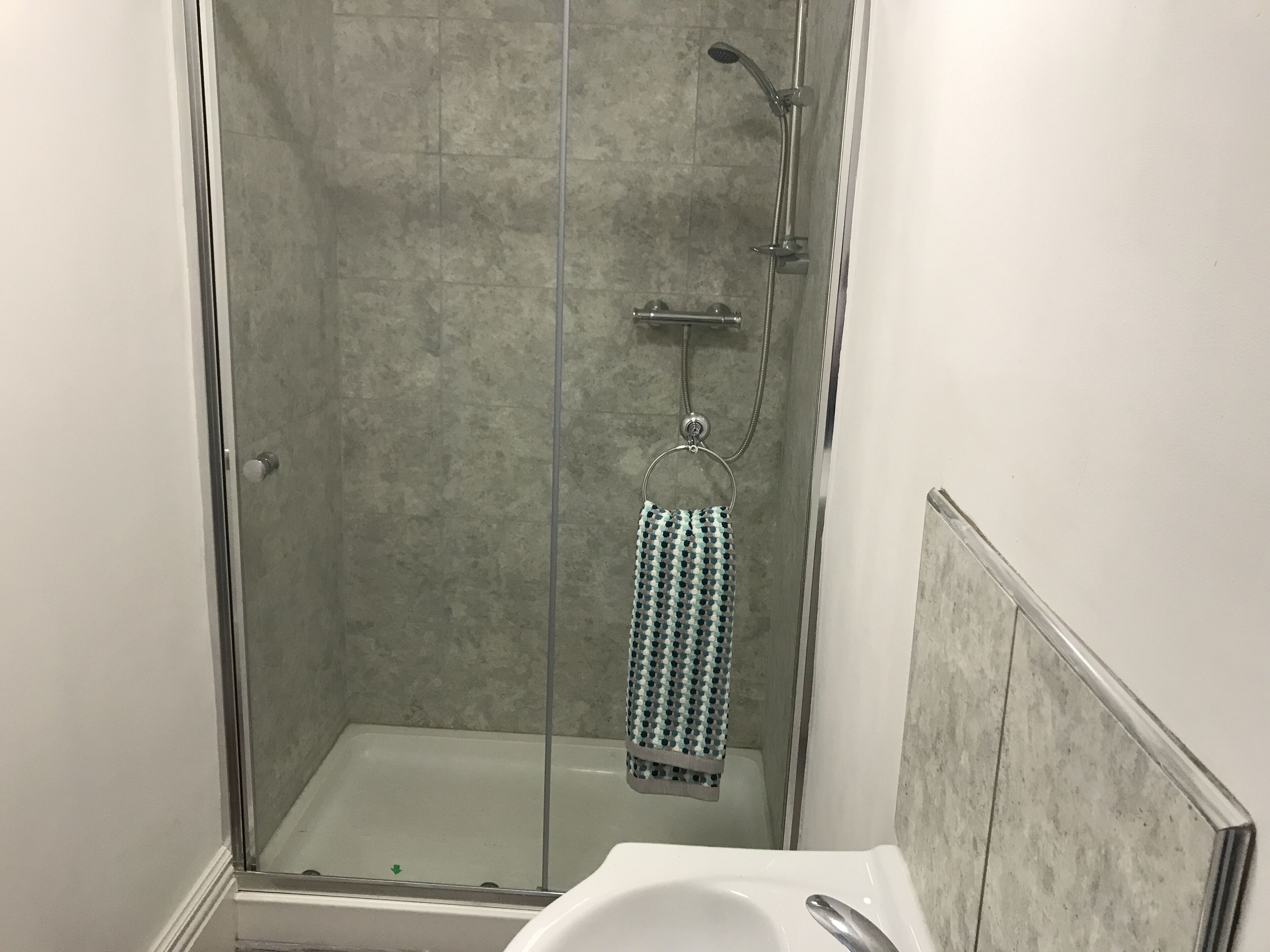 A glass-enclosed shower with a handheld showerhead and a towel rack with a patterned towel.