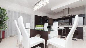 A modern kitchen with dark cabinets, a stainless steel refrigerator, and a glass dining table with white chairs. - Heliko 201 by cocoBR (Playa del Carmen)
