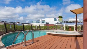 A pool area with a wooden deck, a hot tub, and a view of buildings in the background. - Heliko 201 by cocoBR (Playa del Carmen)