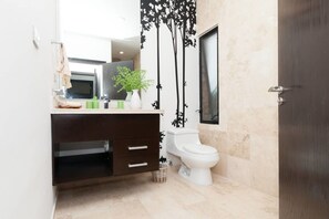 Un baño moderno con tocador de madera oscura, inodoro blanco y un espejo grande sobre el lavamanos.