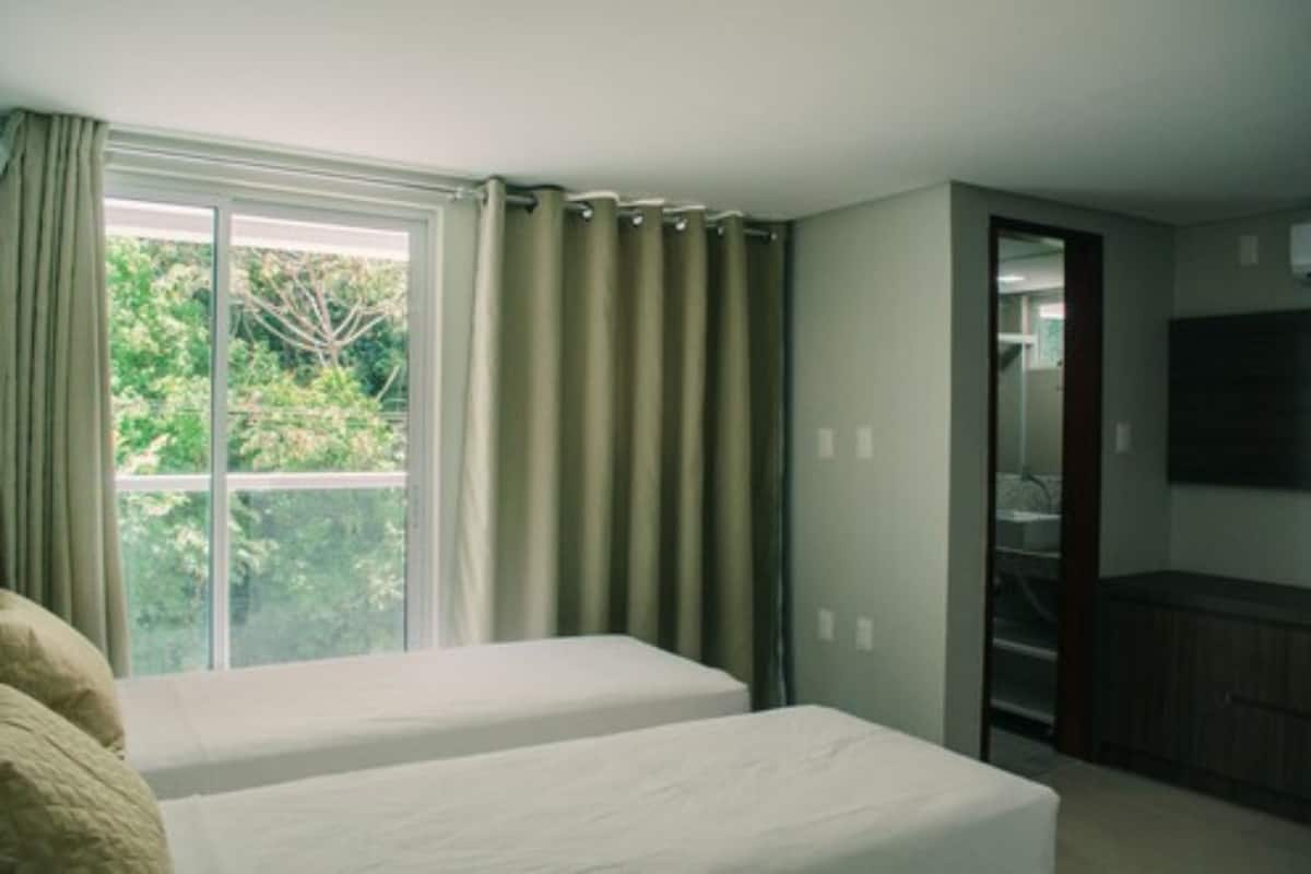 Habitación de hotel con dos camas, un ventanal con cortinas, un televisor en la pared y vistas a zonas verdes.