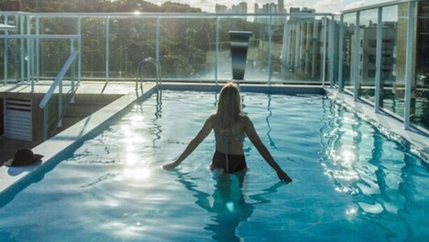 A person in a swimming pool with a cityscape view. - Oriental Praia Hotel (João Pessoa)