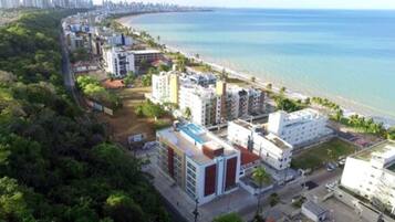 An aerial view of a coastal residential area with buildings, a beach, and a clear view of the ocean.