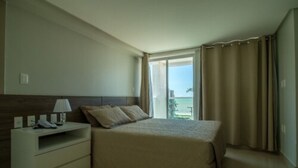 A bedroom with a bed, a bedside table with a lamp, and a view of the outdoors. - Oriental Praia Hotel (João Pessoa)