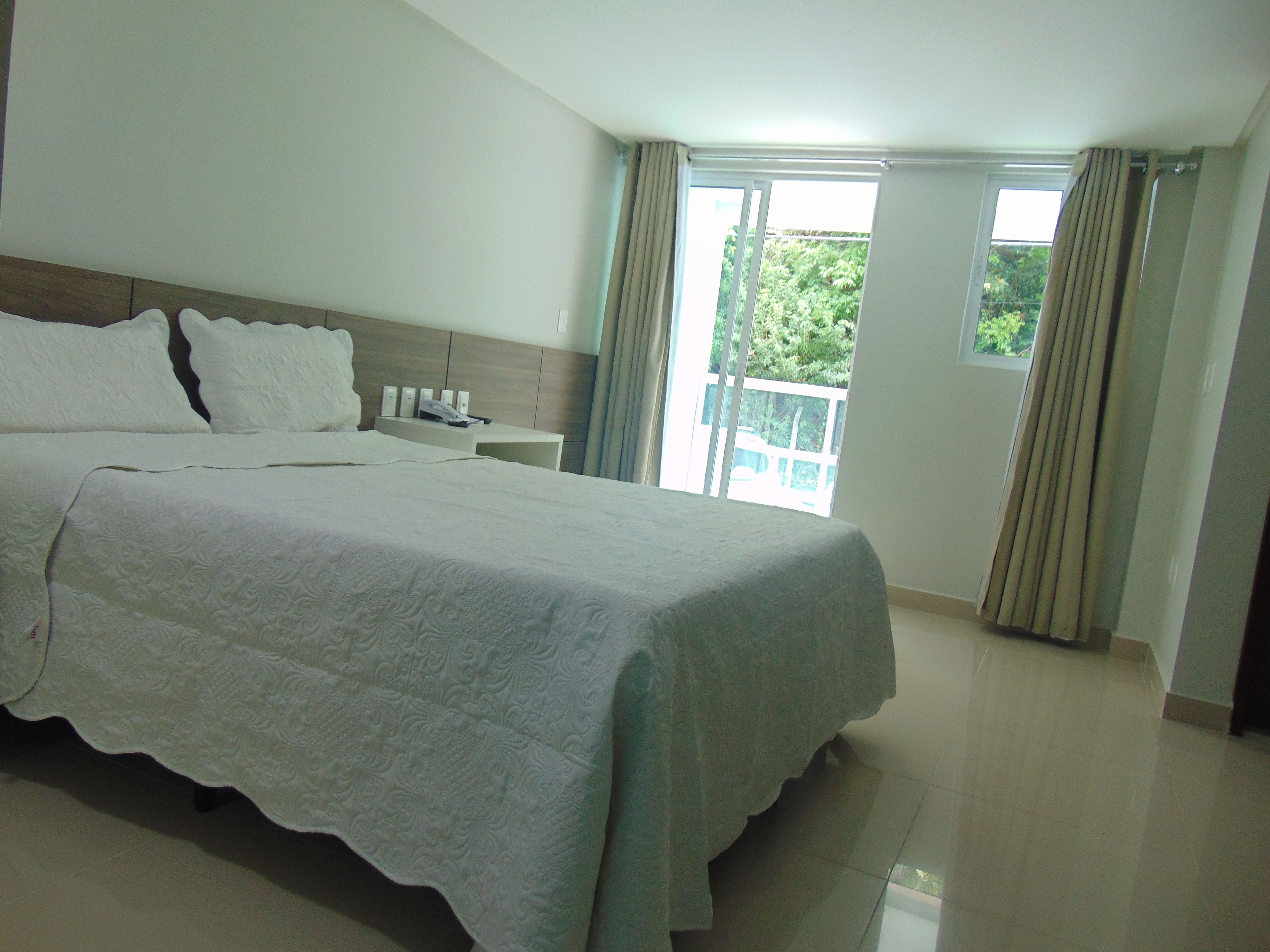 Habitación de hotel con una cama grande, una mesita de noche con teléfono y lámpara, y vista a zonas verdes por la ventana.