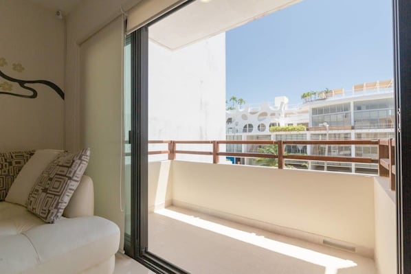 Un balcon avec une balustrade en bois, un canapé blanc agrémenté de coussins à motifs et une vue sur un immeuble moderne doté de balcons.