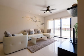 Un salon moderne avec un ensemble de canapés blancs, une table basse et un ventilateur de plafond.