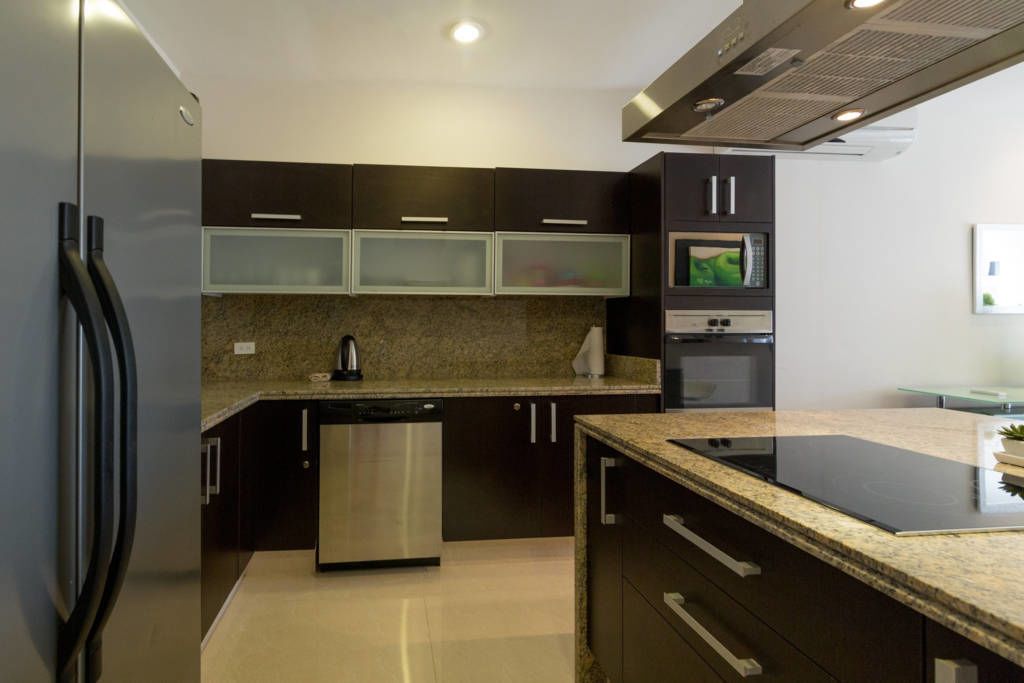 Cozinha moderna com armários escuros, geladeira de aço inoxidável, lava-louças e forno embutido.