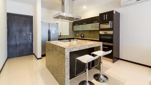 A modern kitchen with granite countertops, stainless steel appliances, and a central island with bar stools. - Heliko 305 by CocoBR (Playa del Carmen)