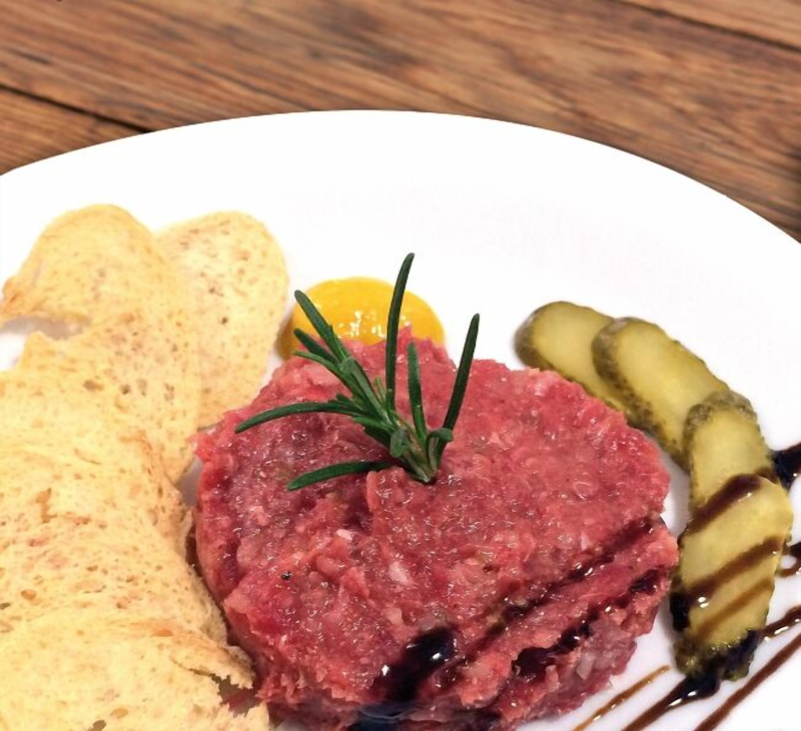 A plate with steak tartare, pickles, and crackers.