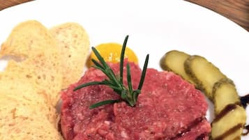 A plate with steak tartare, pickles, and crackers.