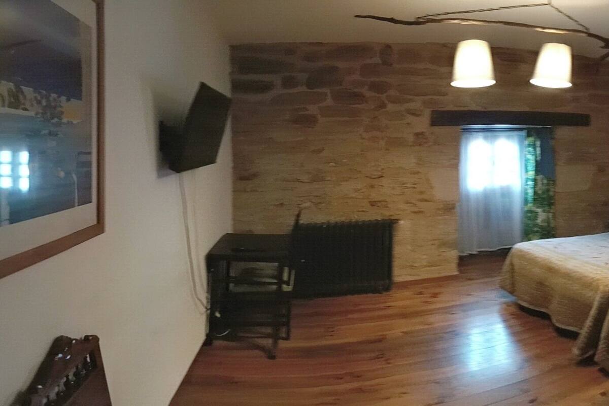 Ein Schlafzimmer mit Steinswand, einem Bett mit Kopfteil, einem kleinen Tisch und einem Fenster mit Vorhängen.