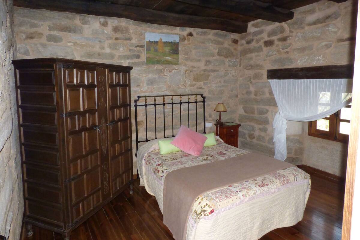Ein rustikaler Raum mit einer Steinwand, einem Holzschrank, einem Bett mit floralem Bettbezug und einem Fenster mit weißem Baldachin.