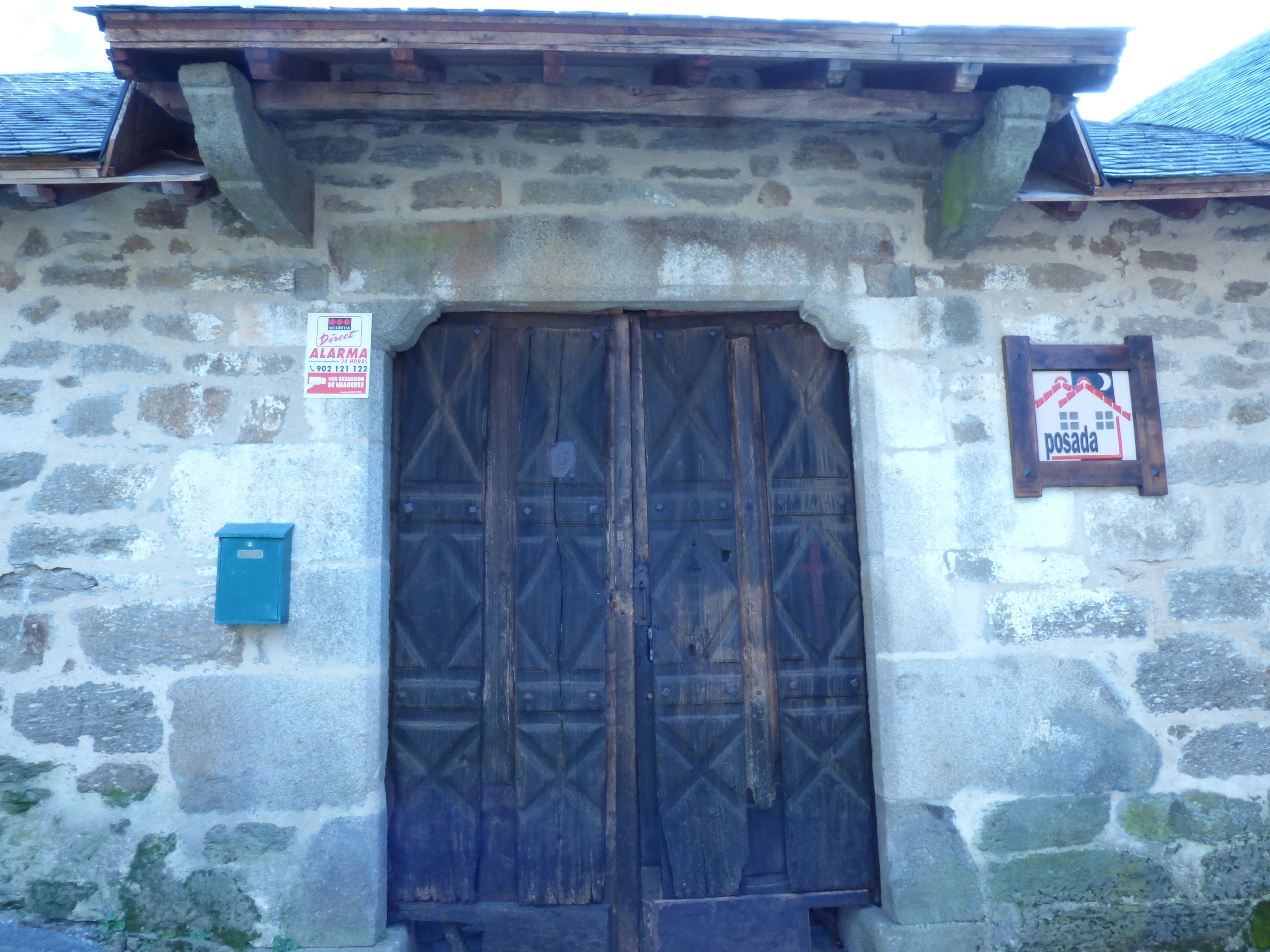 A stone building with a large wooden door and a small signboard.