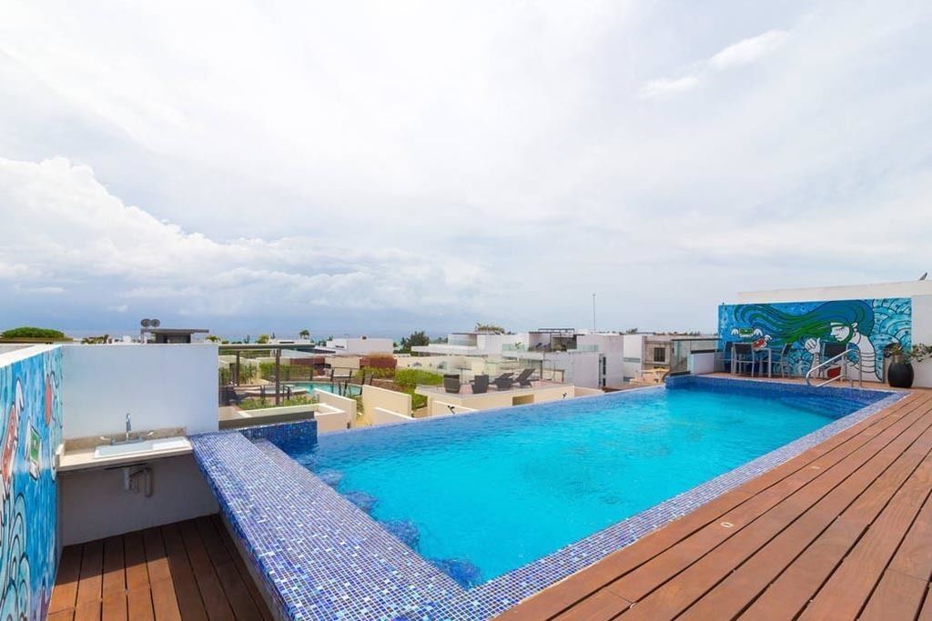 A rooftop swimming pool with a wooden deck and a view of the cityscape.