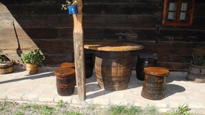 A rustic outdoor seating area with wooden barrels and stools, a wooden table, and potted plants against a stone wall. - Tradicije Čigoč (Sisak)