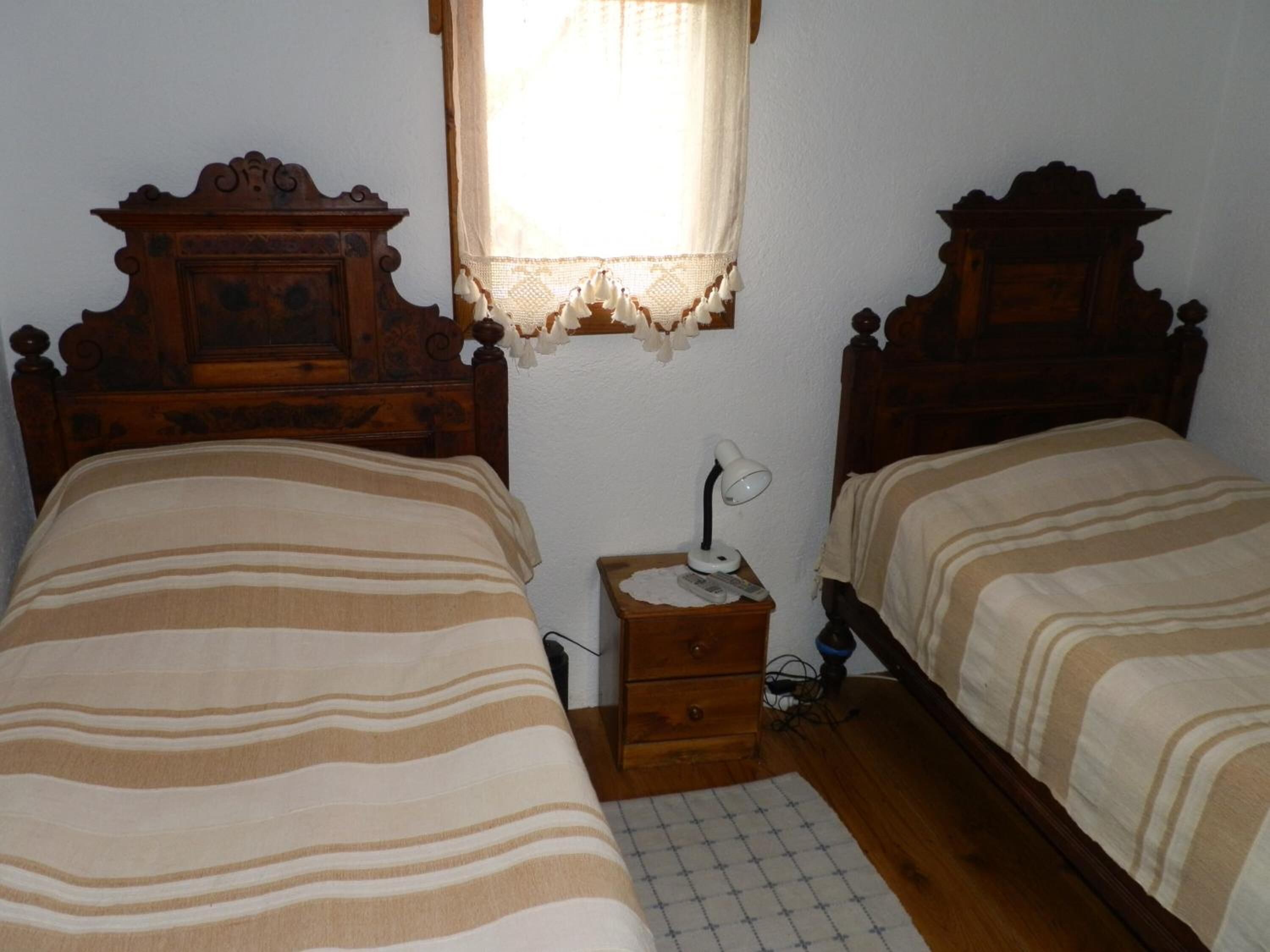 Una camera da letto con due letti in legno, un comodino con una lampada e una finestra con tende in pizzo.