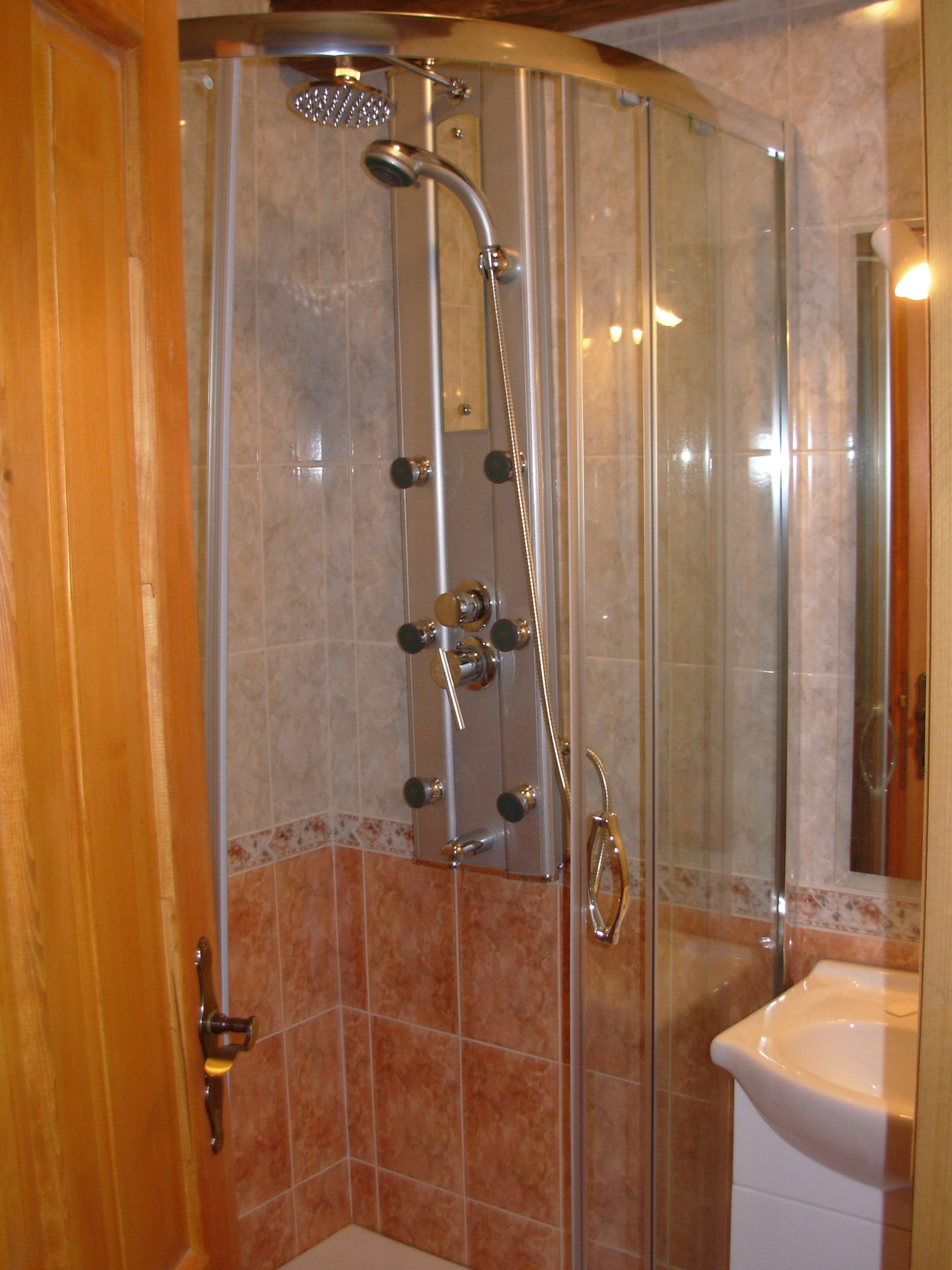 A glass-enclosed shower with a handheld showerhead and multiple controls.
