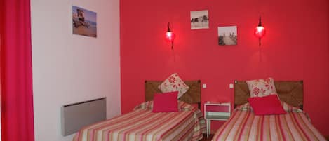 Een kamer met twee bedden, elk voorzien van gestreept beddengoed en rode kussens, een rode muur, en een kleine tafel met een lamp.