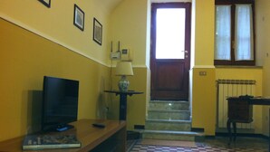 Un pasillo con piso a cuadros, un televisor sobre un soporte de madera, una lámpara sobre una mesita y una puerta que da a otra habitación.