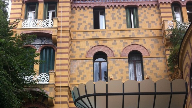 Un edificio de varios pisos con fachada amarilla, contraventanas verdes y balcones ornamentados.