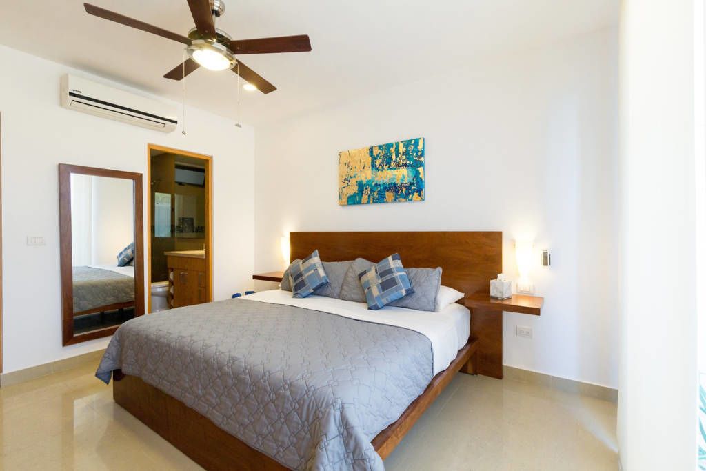 A bedroom with a bed, a ceiling fan, a nightstand, a mirror, and a painting on the wall.