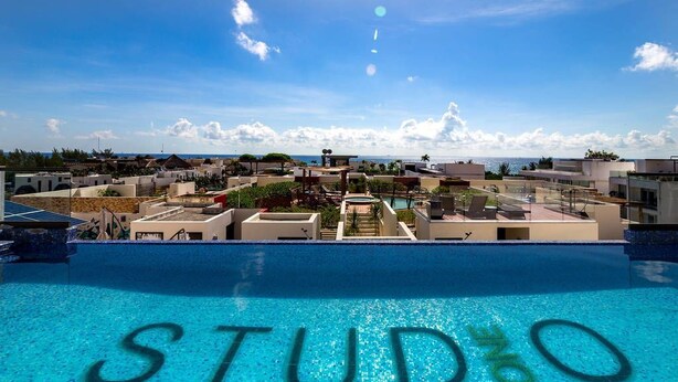 A swimming pool with the word "STUDO" written in the water, surrounded by buildings and a clear sky. - Studio one 208 by CocoBR (Playa del Carmen)