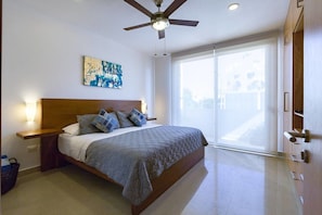 Una camera da letto con un letto, una ventola a soffitto, un'ampia finestra e un'opera d'arte appesa al muro.