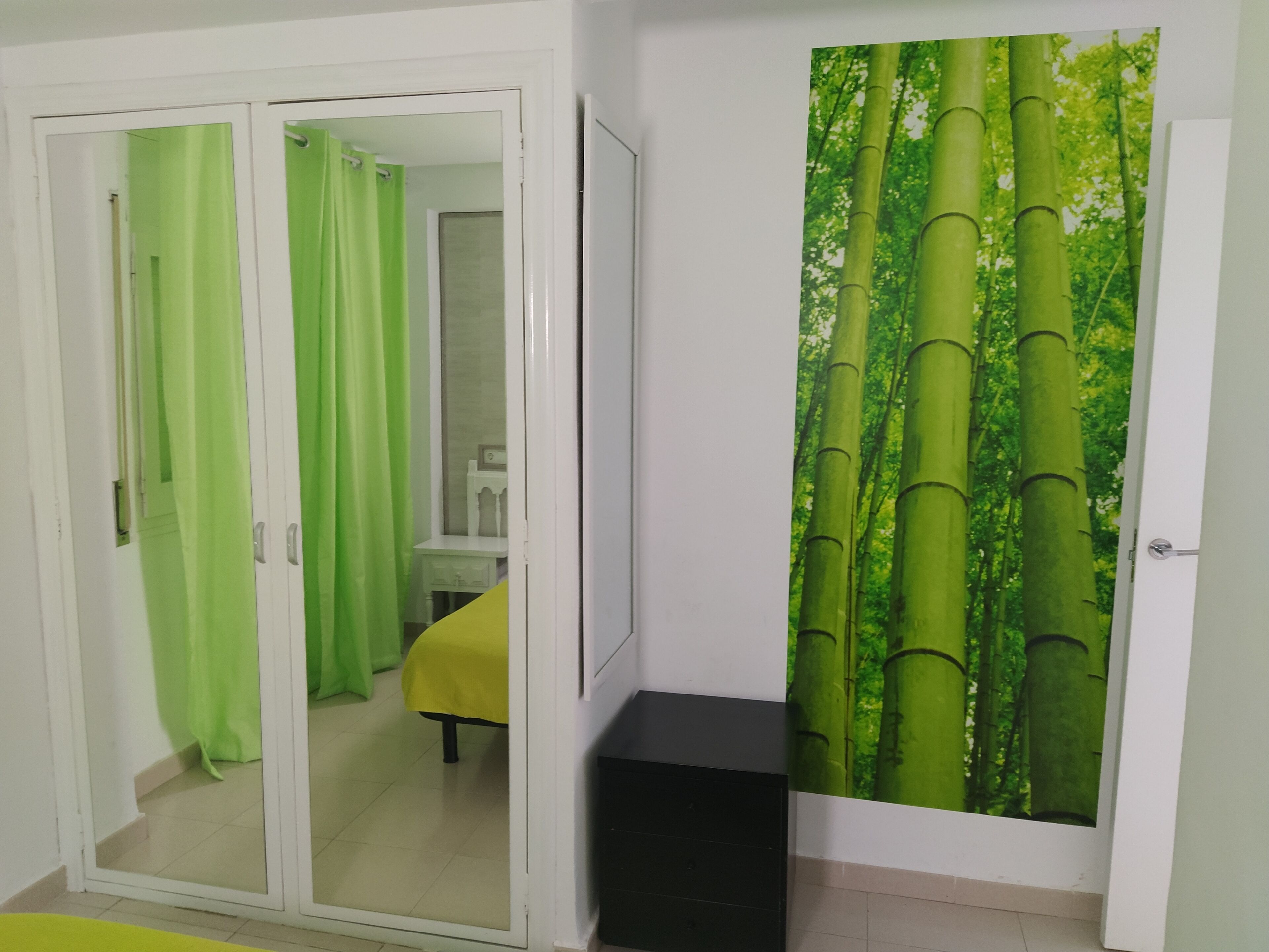 A room with a sliding door leading to a bathroom, a bed with a yellow bedspread, and a wall with a bamboo forest mural.
