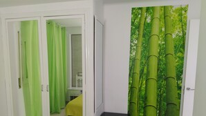 A room with a sliding door leading to a bathroom, a bed with a yellow bedspread, and a wall with a bamboo forest mural.