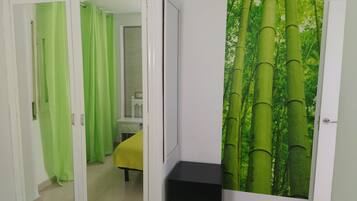 A room with a sliding door leading to a bathroom, a bed with a yellow bedspread, and a wall with a bamboo forest mural.