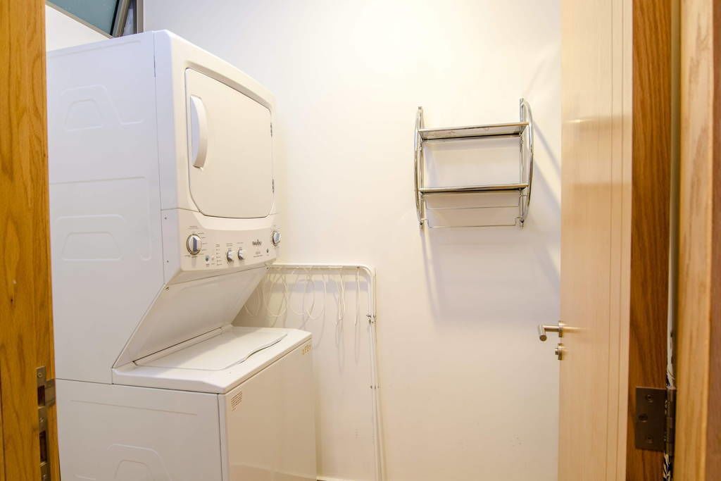 A laundry room with a stacked washer and dryer, a metal drying rack, and a door.