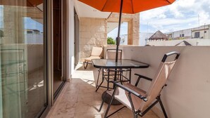 A balcony with a glass door, a table with chairs, and an orange umbrella. - Studio one 303 by CocoBR (Playa del Carmen)