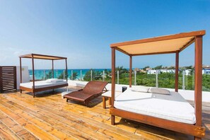 Een houten terras met twee houten bedden en een lounge stoel, met uitzicht op een heldere blauwe zee en groen.