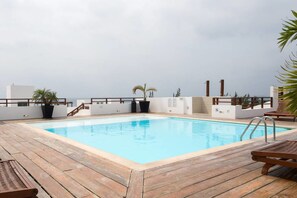Une piscine sur le toit, avec une terrasse en bois, des palmiers et une vue sur l’océan.