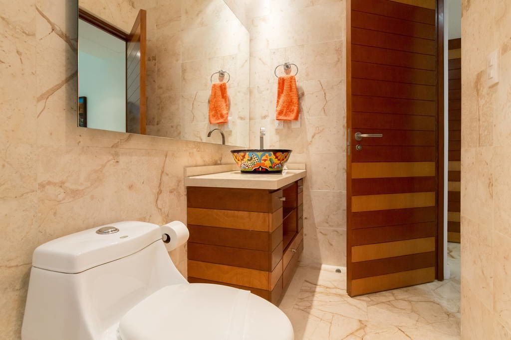 A bathroom with a toilet, a sink with a colorful bowl, and a mirror. There are two towels hanging on hooks above the sink.