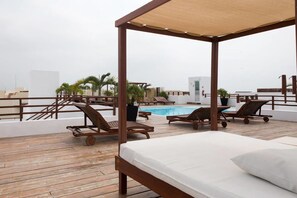 Un espace piscine aménagé sur le toit, avec une terrasse en bois, des chaises longues et une structure en forme de tonnelle.